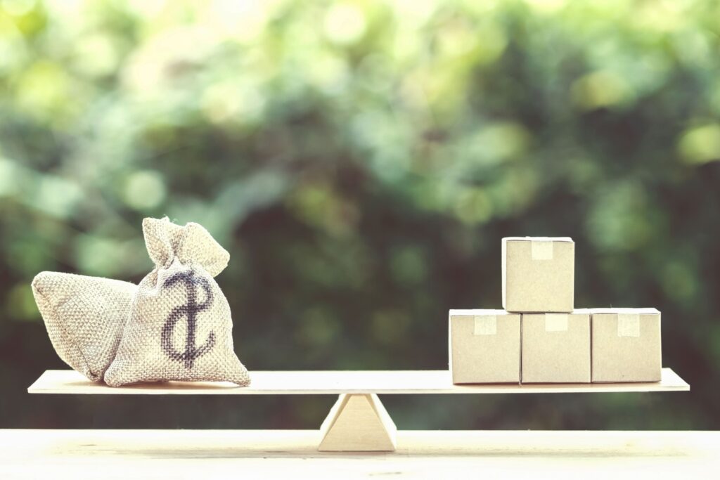 Saco de dinheiro e caixas equilibrados em uma balança, representando a diversificação de uma carteira