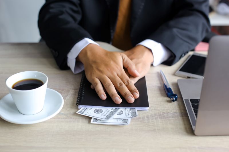 Um homem esconde com as mãos uma agenda com algumas notas de dólar aparecendo.