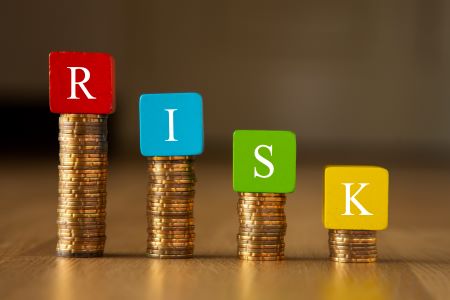 Cubos de madeiras com as letras R, I, S, K (risco, em inglês), sobre pilhas de moedas representando a gestão de risco