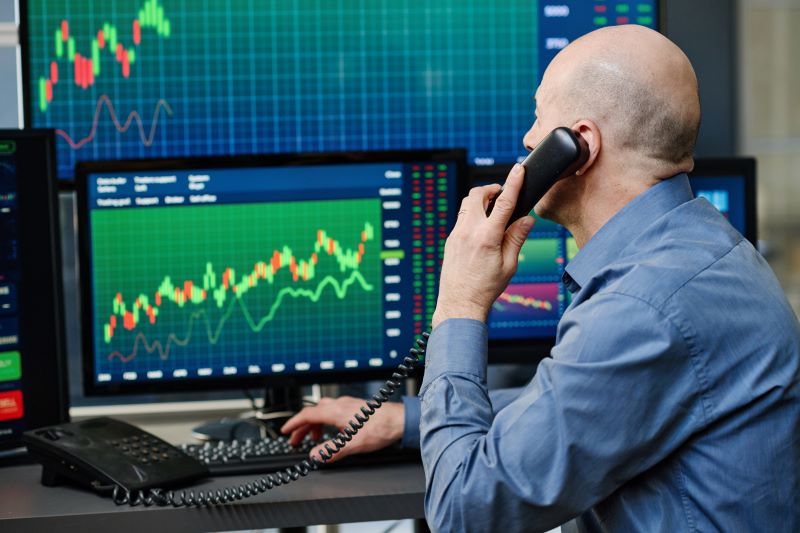 Investidor acompanhando o IBRx50 enquanto fala ao telefone com assessor de investimento