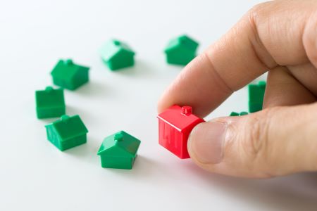 Mão adicionando uma casinha de brinquedo vermelha, em um conjunto de casinhas verdes, representando investimento no Mercado de FIIs