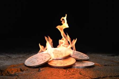 Moedas pegando fogo, representando a queima do poder de compra ocasionado pelo IGPM