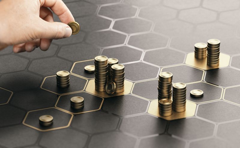 Mão separando moedas em blocos distintos, representando estratégias de investimentos para potencializar rendimentos.