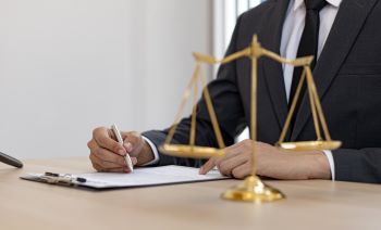 Homem escrevendo em documento em frente a uma balança da justiça