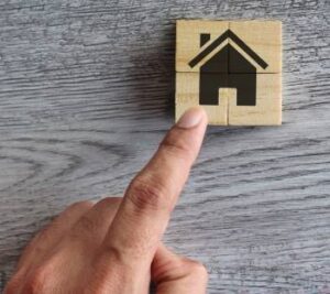 Mão apontando para uma casa pintada em cubos de madeira, representando o que são fundos imobiliários