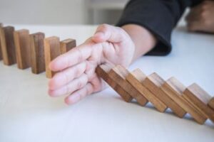 mão parando queda de fileira de dominós, representando coberturas de riscos 