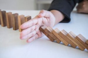 mão parando queda de fileira de dominós, representando coberturas de riscos