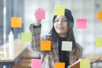 Mulher organizando postits em parede de vidro, representando os tipos de FIIs