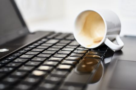 Xícara de café derramando sobre um teclado, representando erros ao operar triângulos