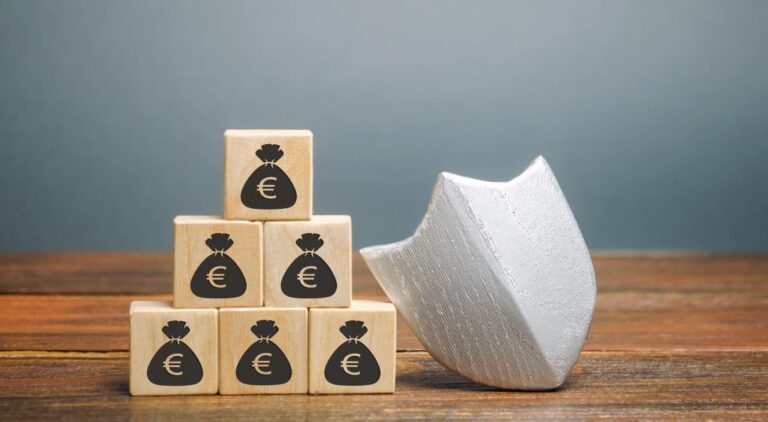 Escudo branco ao lado de cubos de madeira com ícone de saco de dinheiro, representando investimento seguro