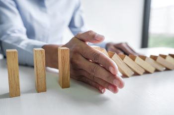 Mão impedindo uma fila de dominós de continuar a queda, representando controle de risco